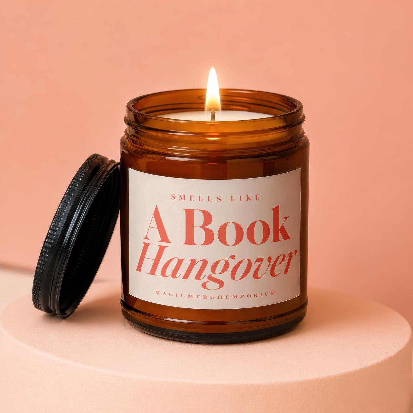 Amber jar candle with lit wick, reads "Smells Like A Book Hangover".