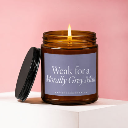 Amber glass candle with lit wick and black lid, says "Weak for a Morally Grey Man."