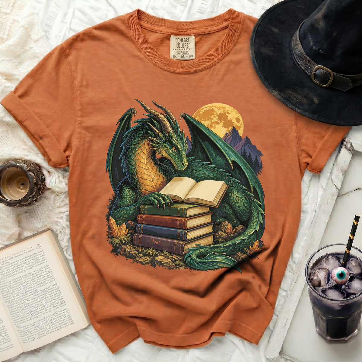Orange t-shirt with a green dragon reading books under a full moon.