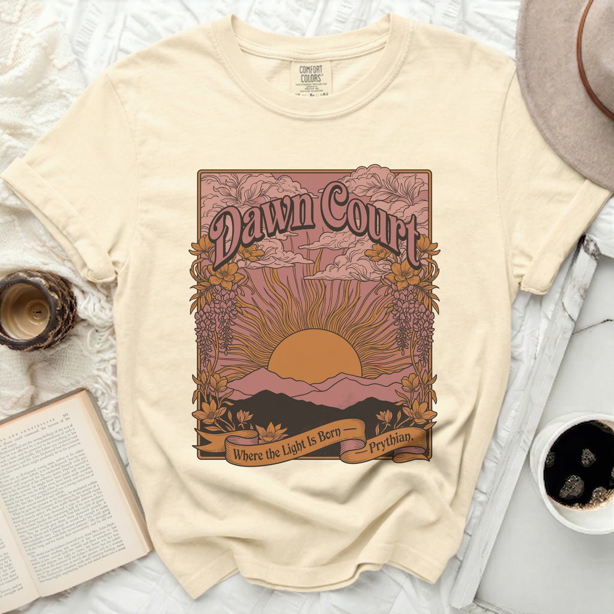 Cream t-shirt with "Dawn Court" graphic featuring a sunrise over mountains and text "Where the Light Is Born - Prythian".