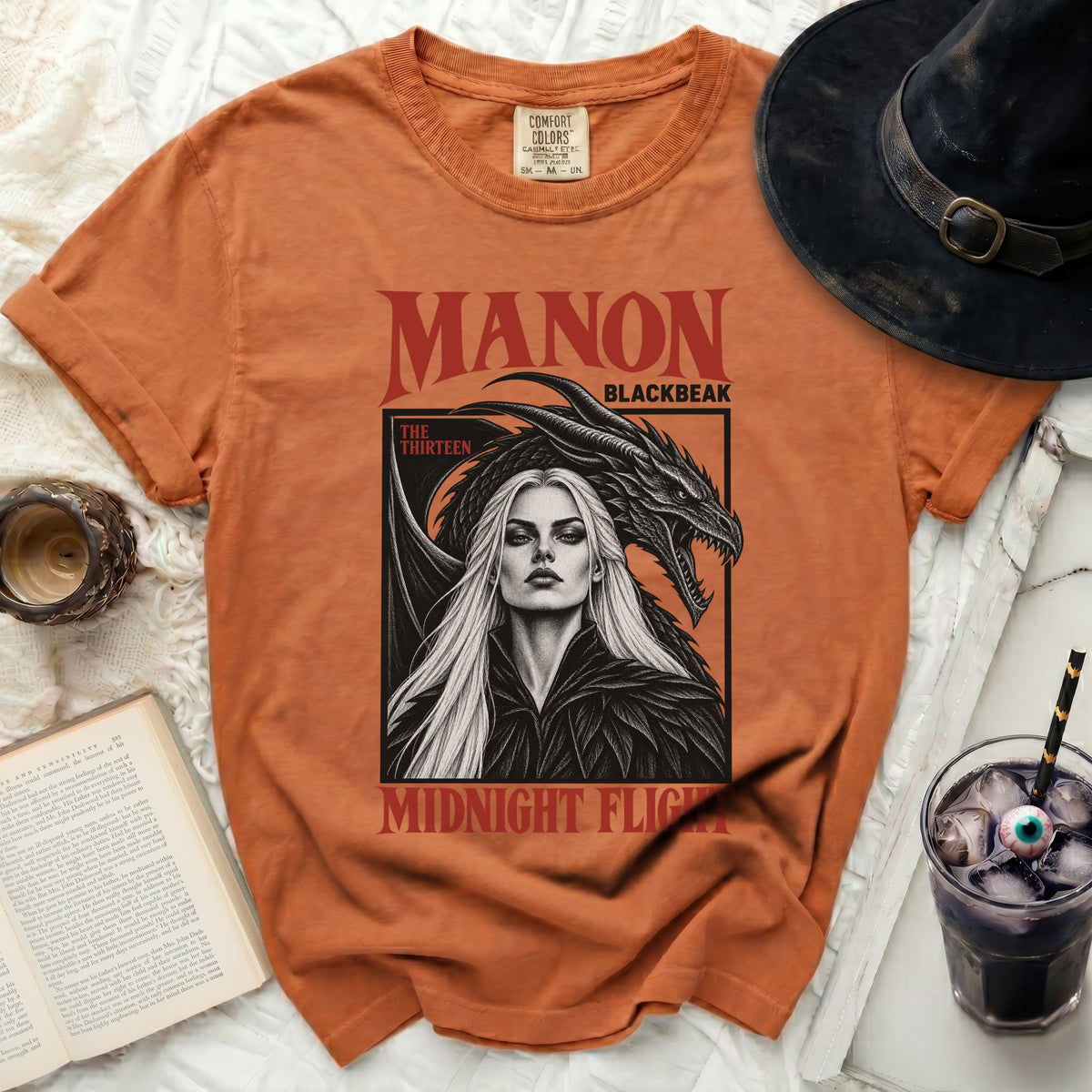 Orange t-shirt featuring "MANON BLACKBEAK THE THIRTEEN MIDNIGHT FLIGHT" text with dragon art.