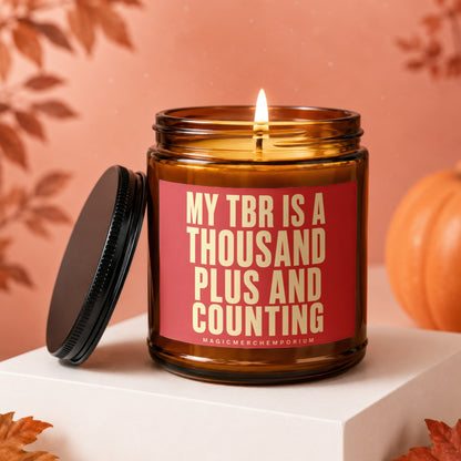 Amber glass candle with lit wick and red label reading "MY TBR IS A THOUSAND PLUS AND COUNTING".