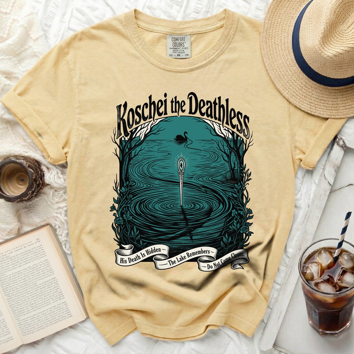 Yellow t-shirt with a graphic of Koschei the Deathless, a swan, and a sword in a lake.