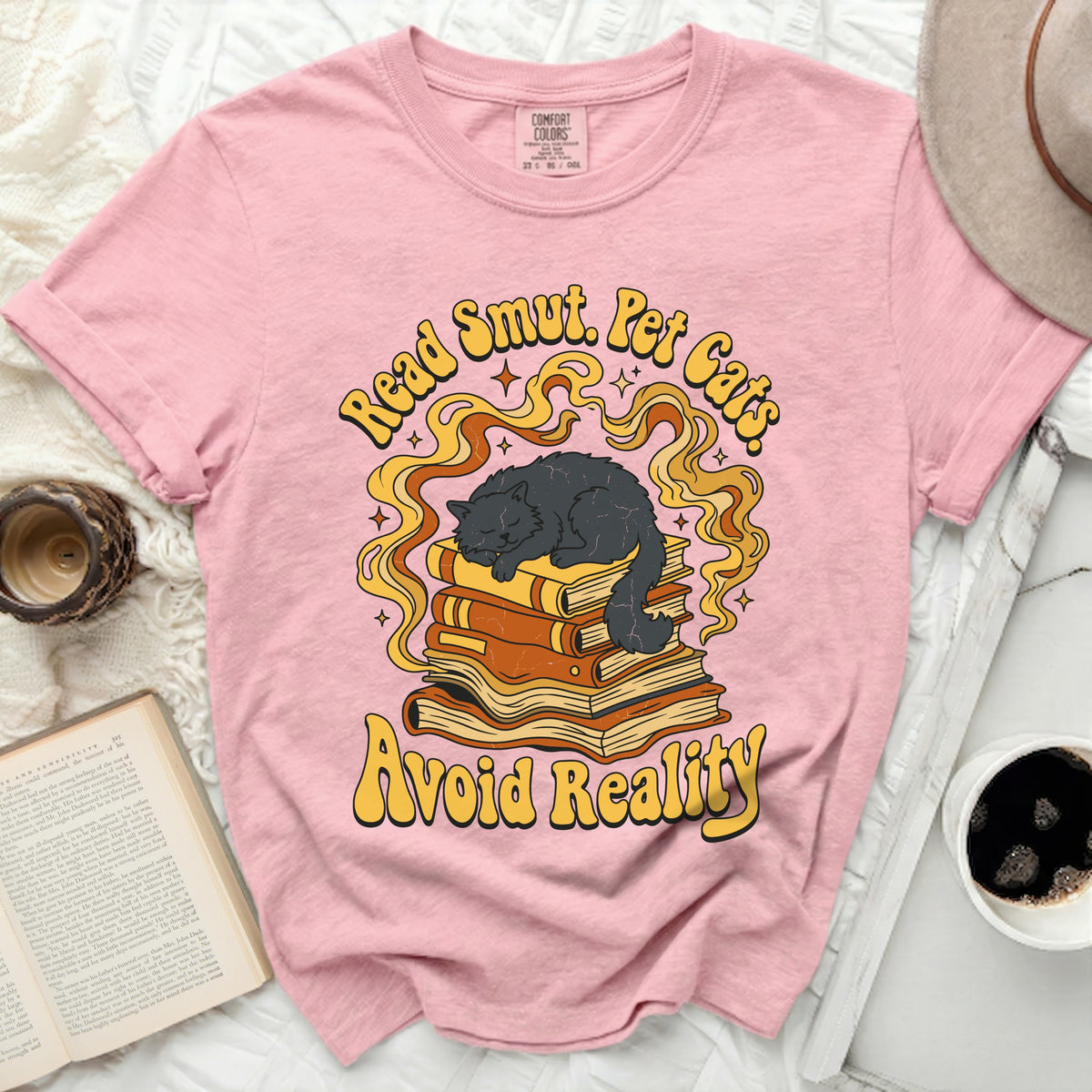 Pink t-shirt with graphic of black cat sleeping on books, "Read Smut. Pet Cats. Avoid Reality."