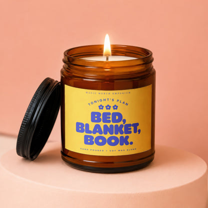 Amber jar candle with lit flame, yellow label reads "Tonight's Plan Bed, Blanket, Book."