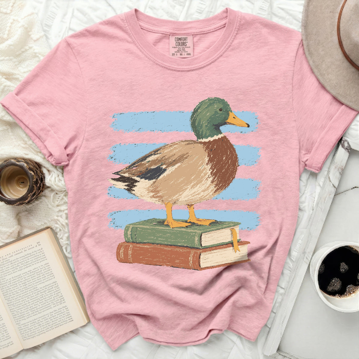 Pink t-shirt with a mallard duck illustration standing on books.