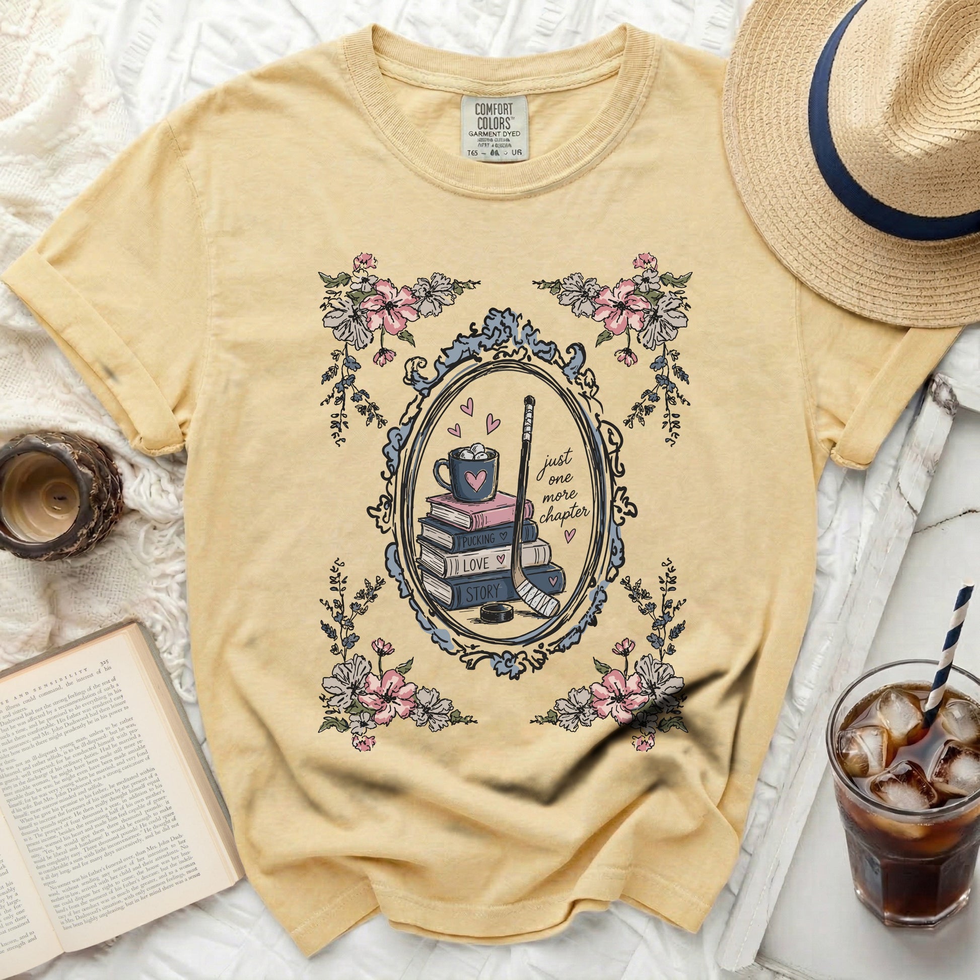Yellow t-shirt with floral frame, hockey stick, book stack, and "just one more chapter" text.