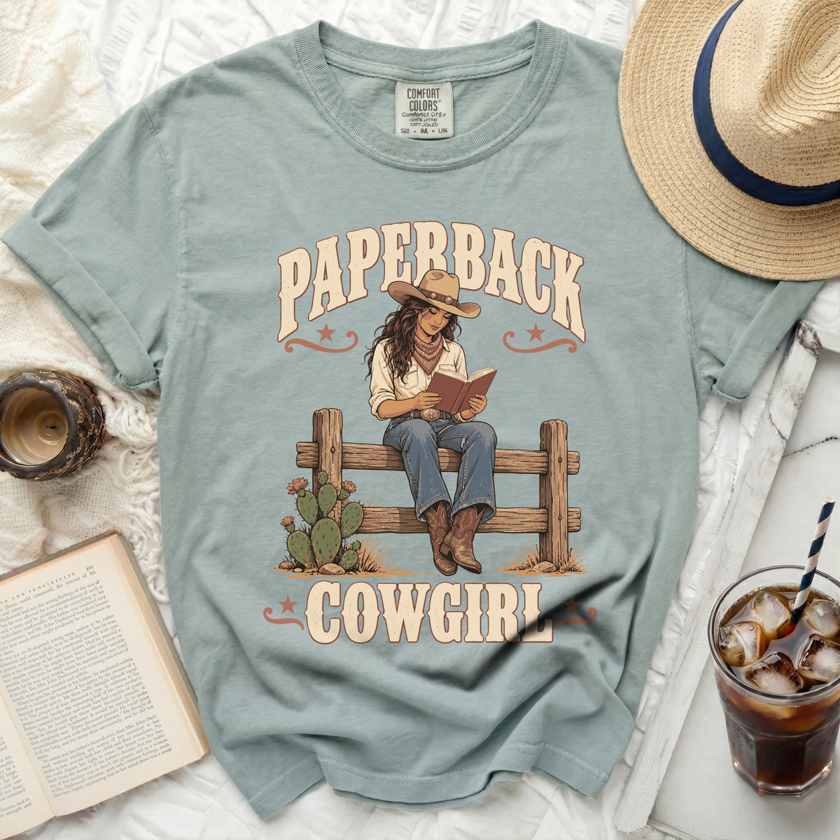 "Paperback Cowgirl" graphic on a light blue t-shirt with a woman reading.