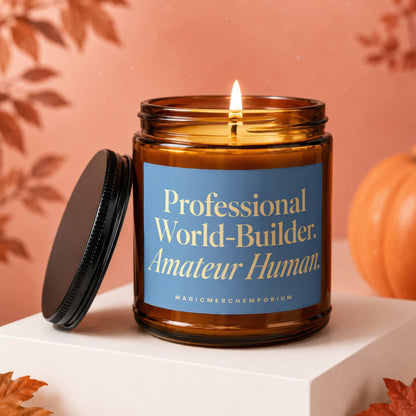 Amber glass candle with lit wick and blue label reading "Professional World-Builder. Amateur Human."