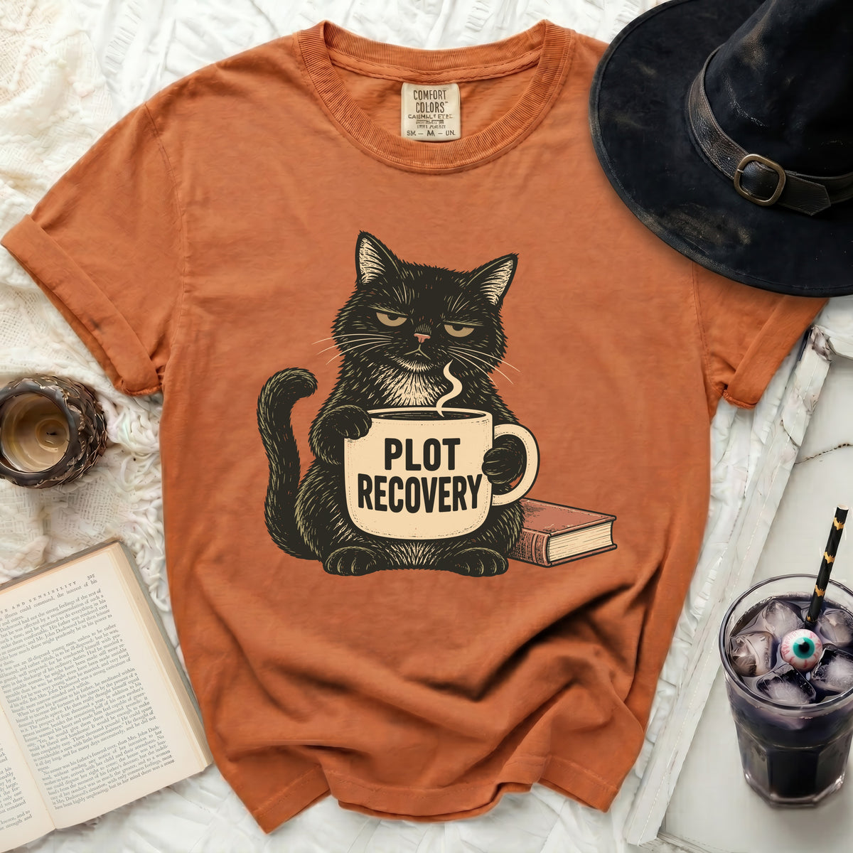 Black cat holding a mug that says "PLOT RECOVERY" next to a book.