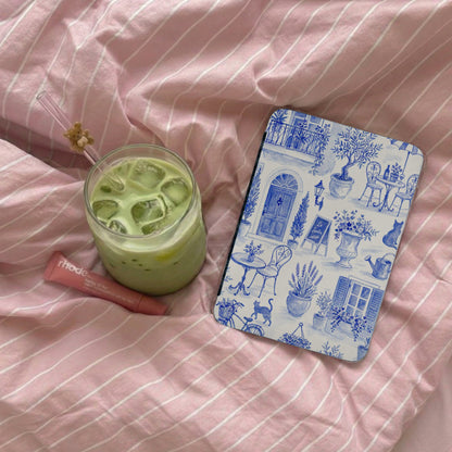 Iced matcha latte, Rhode lip balm, and blue toile notebook on pink striped fabric.
