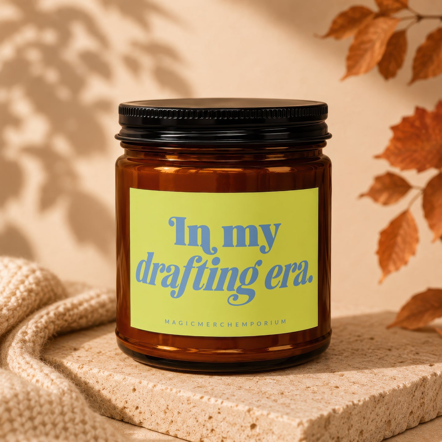 Amber glass candle with "In my drafting era." text on a neon yellow label.