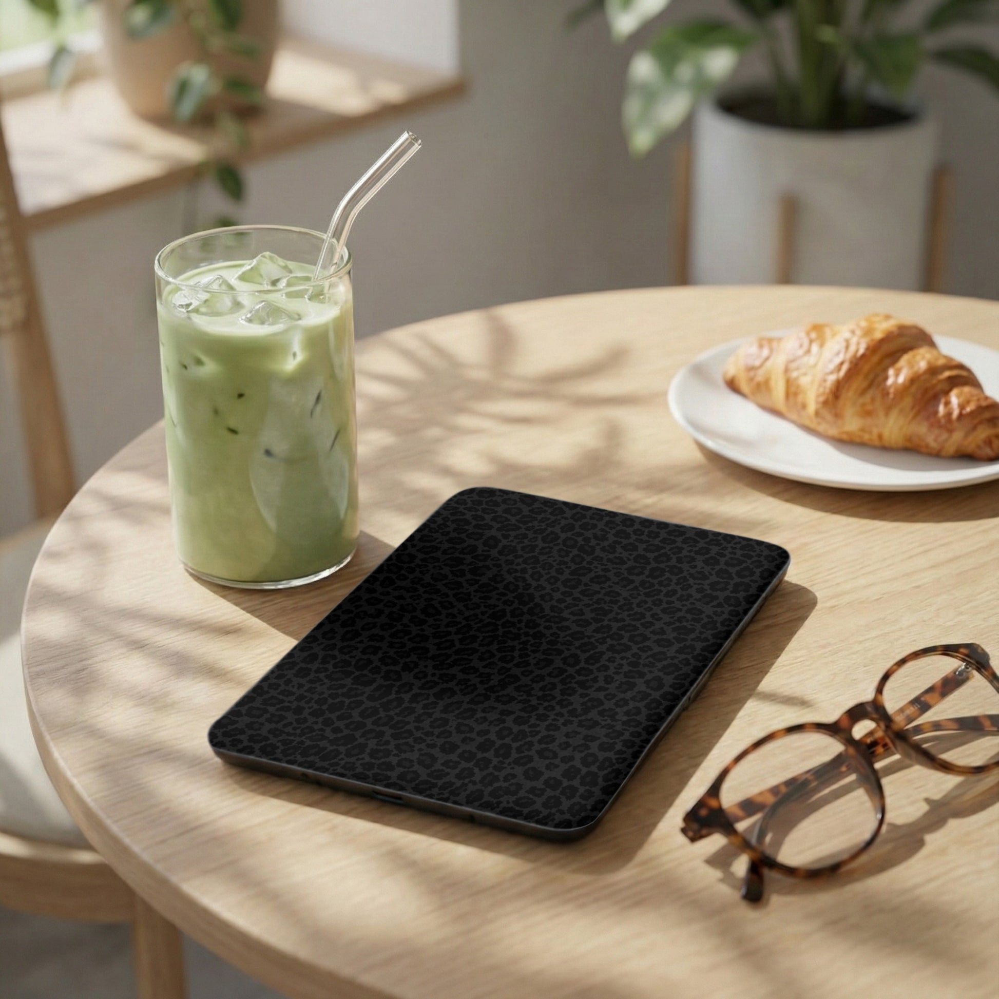 Black leopard print tablet case on a wooden table with iced matcha and croissant