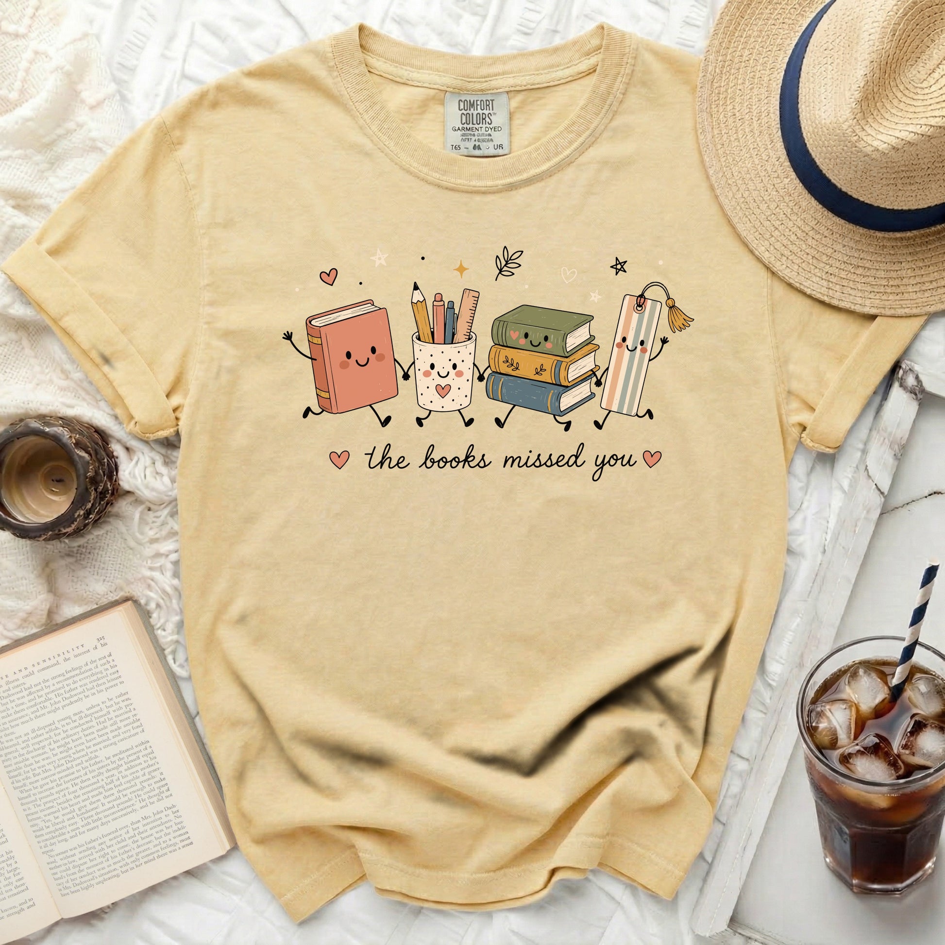 Yellow t-shirt with cartoon books, cup, and bookmark reading "the books missed you".