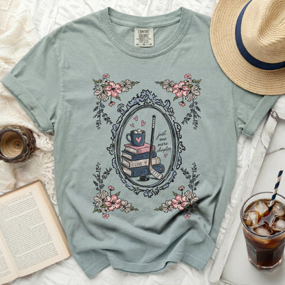 Shirt with floral frame, hockey stick, mug, and "just one more chapter" text.