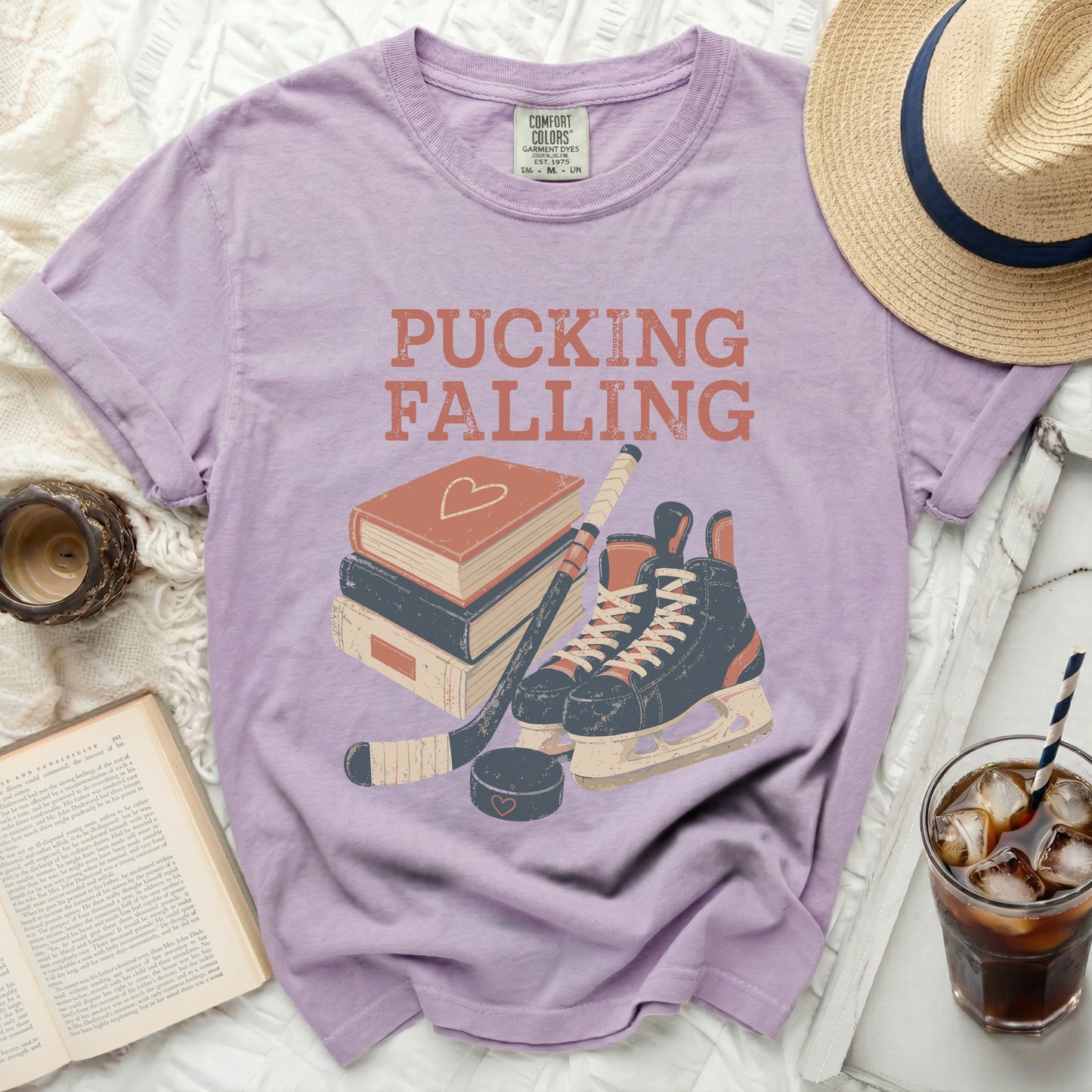Purple t-shirt with "Pucking Falling" text, ice skates, hockey stick, and books.