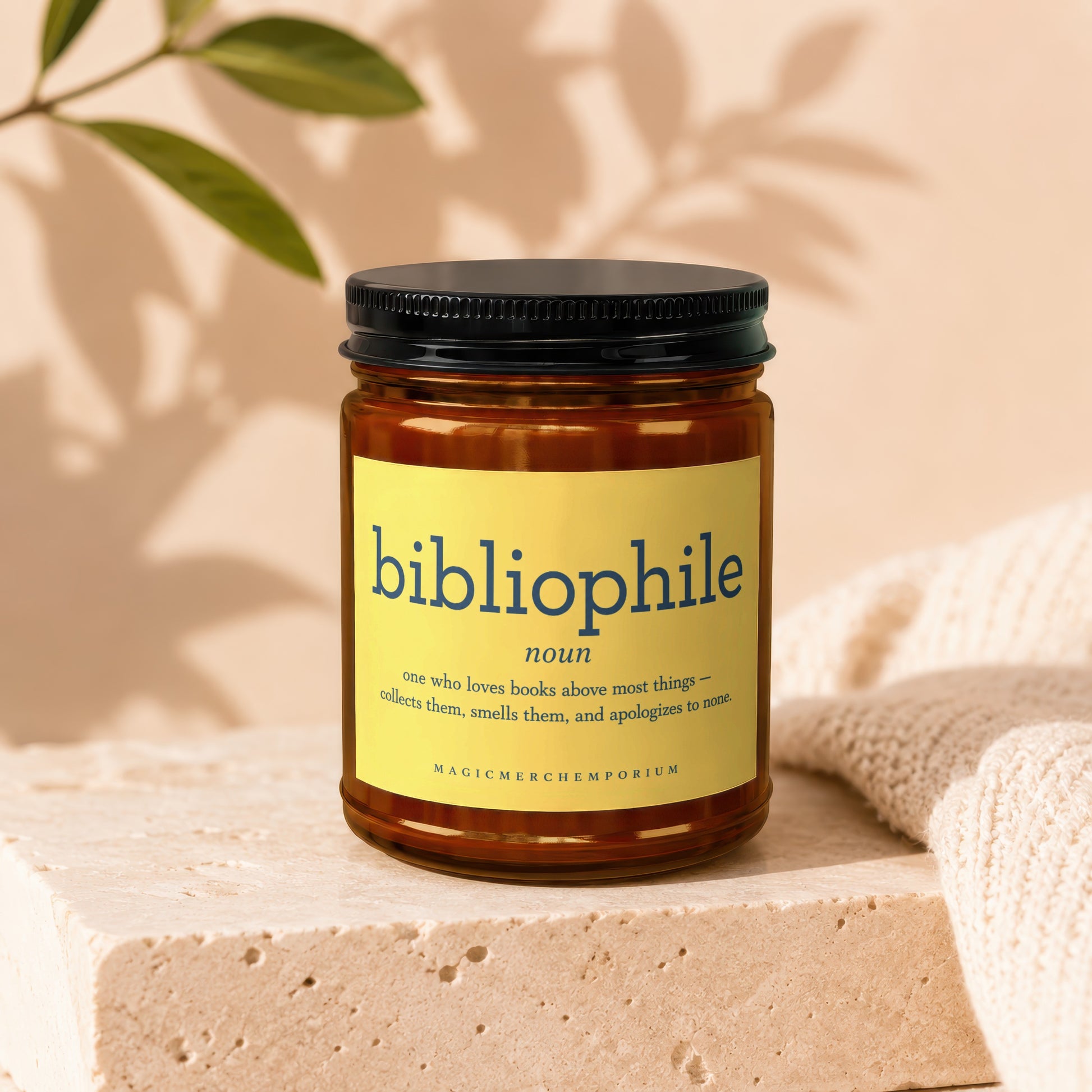 Amber jar candle with yellow label defining "bibliophile" and brand "MagicMerchempirium."