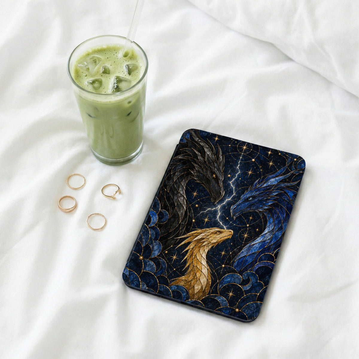 Case with three dragons, lightning, and stars, next to iced matcha drink and rings.