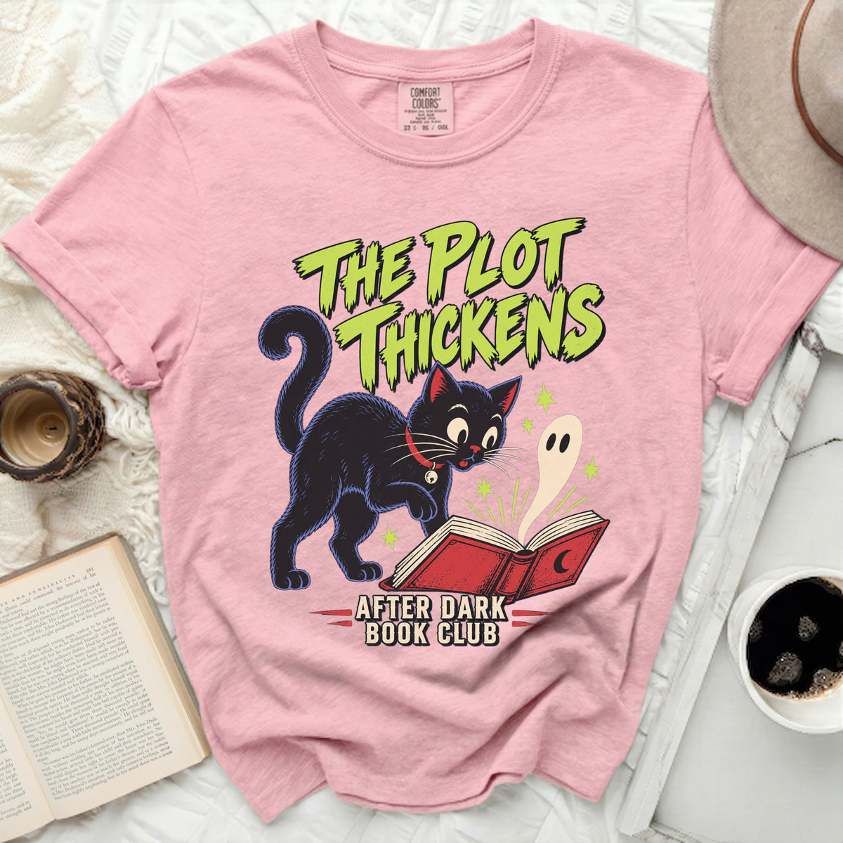 Pink t-shirt with black cat reading a book and ghost, "The Plot Thickens" text.