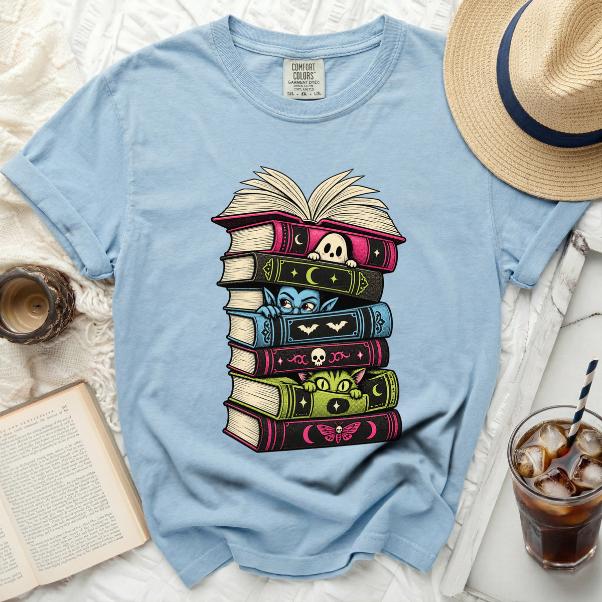 Light blue t-shirt with stack of spooky books featuring ghost, vampire, cat, and moth designs.