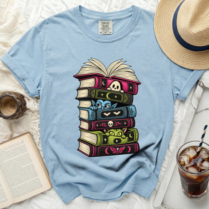 Light blue t-shirt with stack of spooky books featuring ghost, vampire, cat, and moth designs.