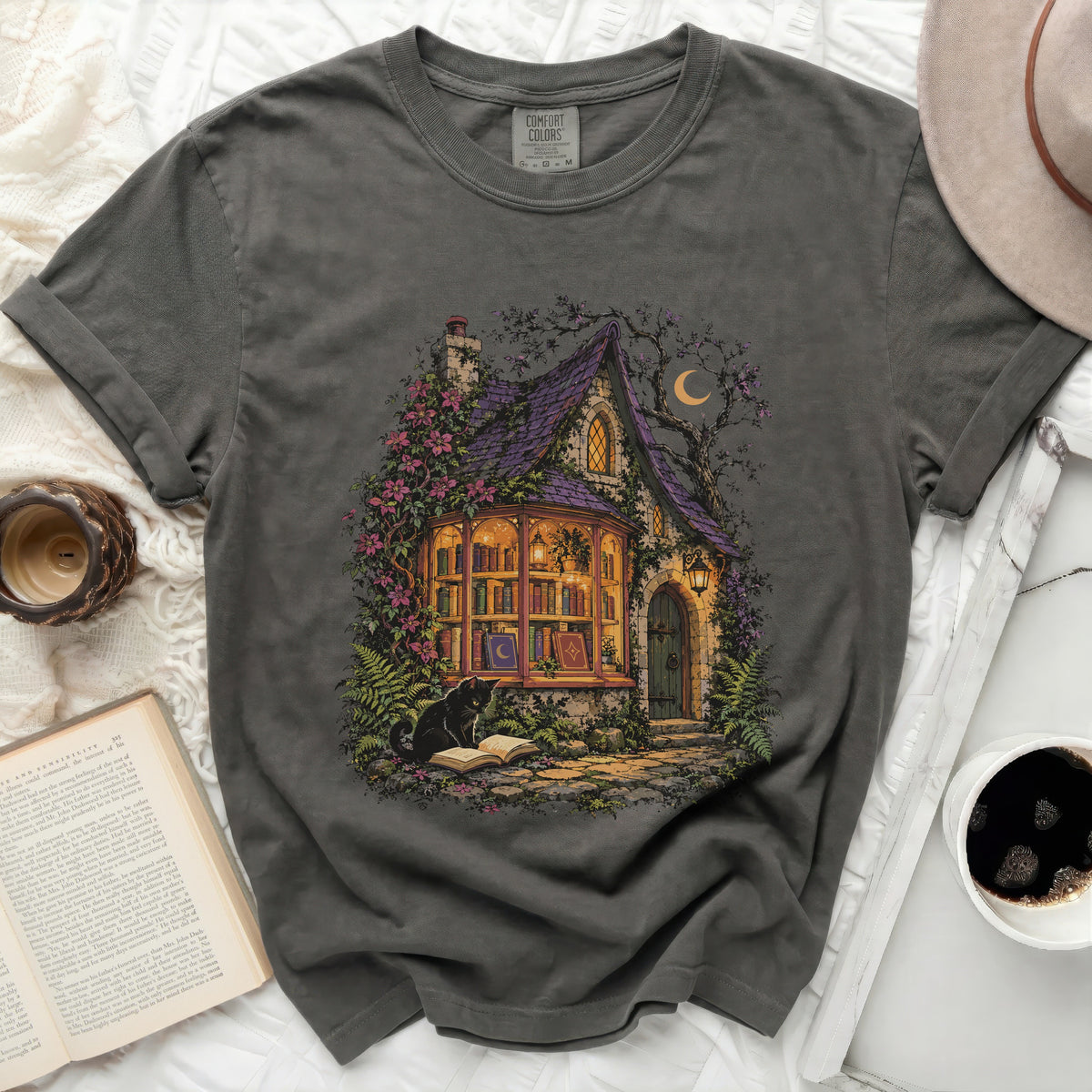 Dark grey t-shirt with a graphic of a witch's cottage, black cat, and books.