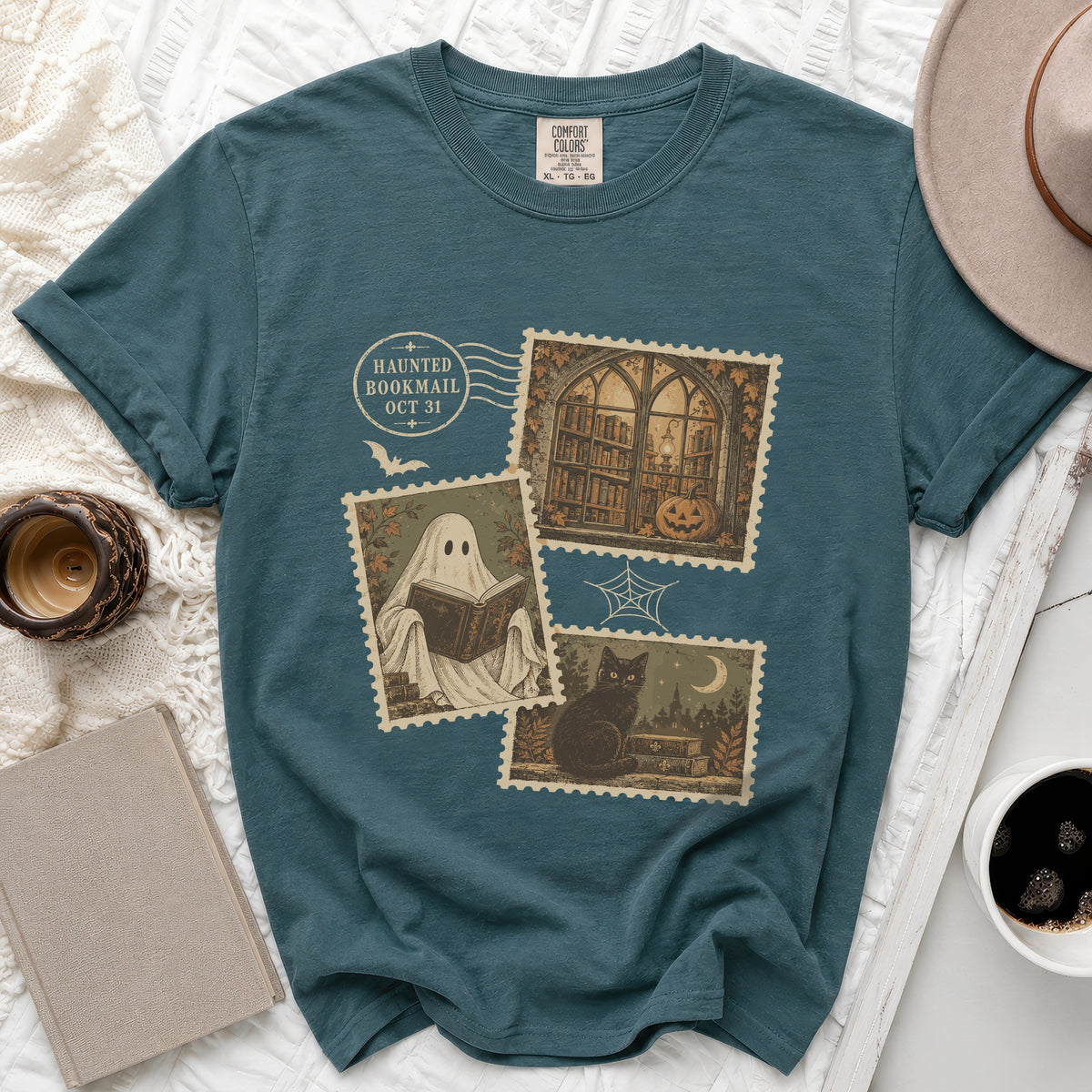 Teal t-shirt with "Haunted Bookmail Oct 31" stamps featuring a ghost reading, library, and black cat.