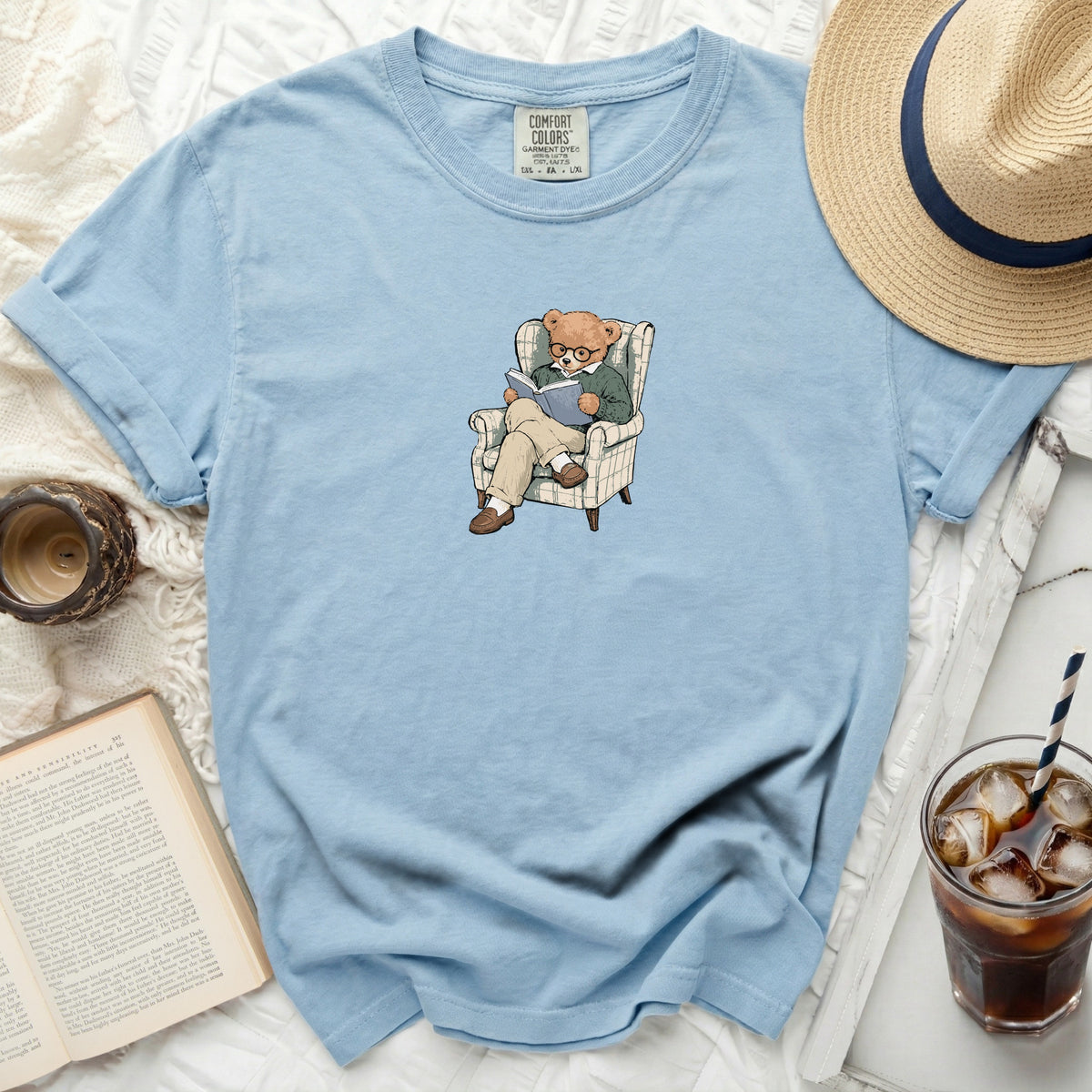 Light blue t-shirt with a teddy bear reading in a chair graphic.