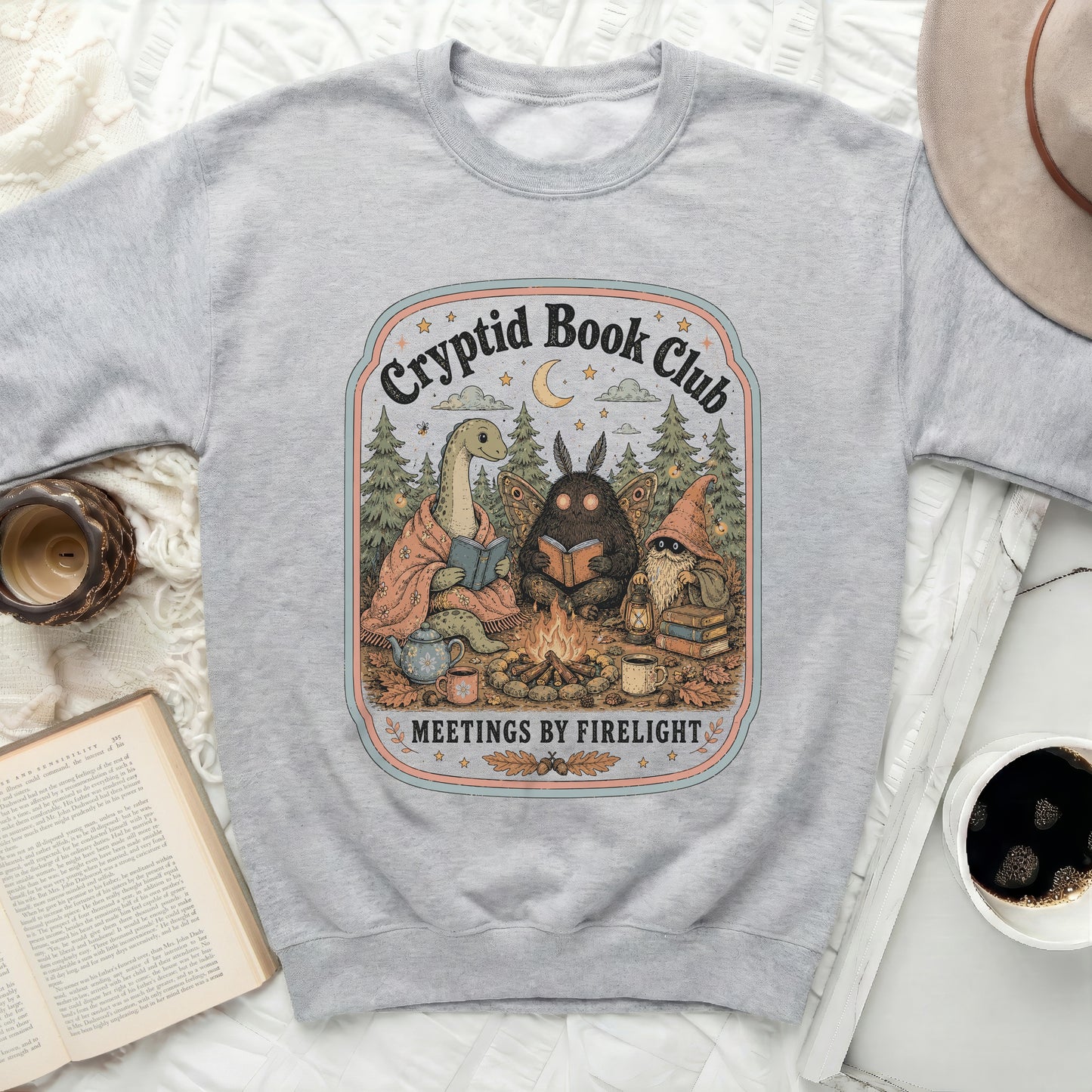 Gray sweatshirt with "Cryptid Book Club Meetings by Firelight" illustration.