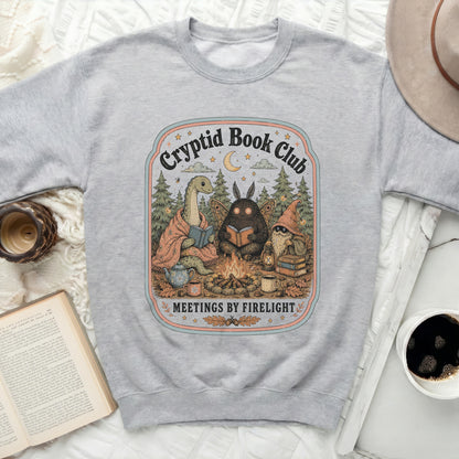Gray sweatshirt with "Cryptid Book Club Meetings by Firelight" illustration.