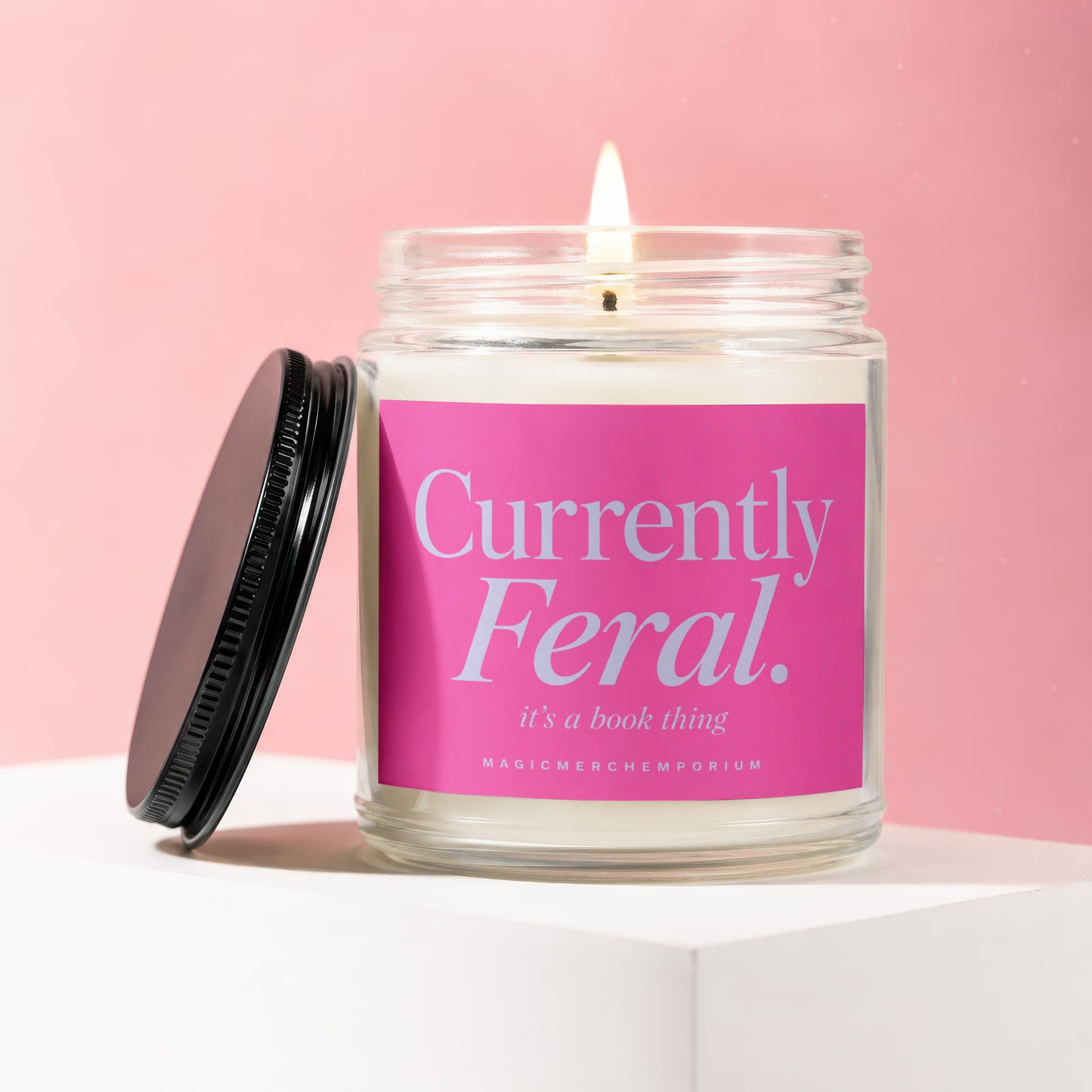 Lit candle in glass jar with pink label reading "Currently Feral. it's a book thing."