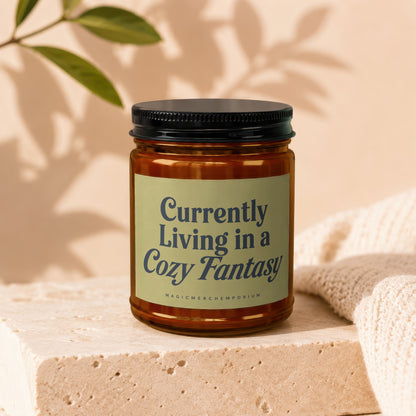 Amber jar candle with "Currently Living in a Cozy Fantasy" text.