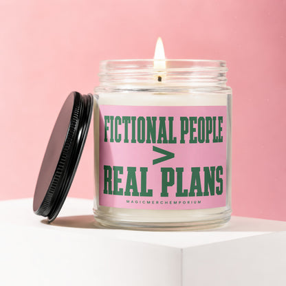 Glass candle with lit flame and black lid, featuring pink label with green text.