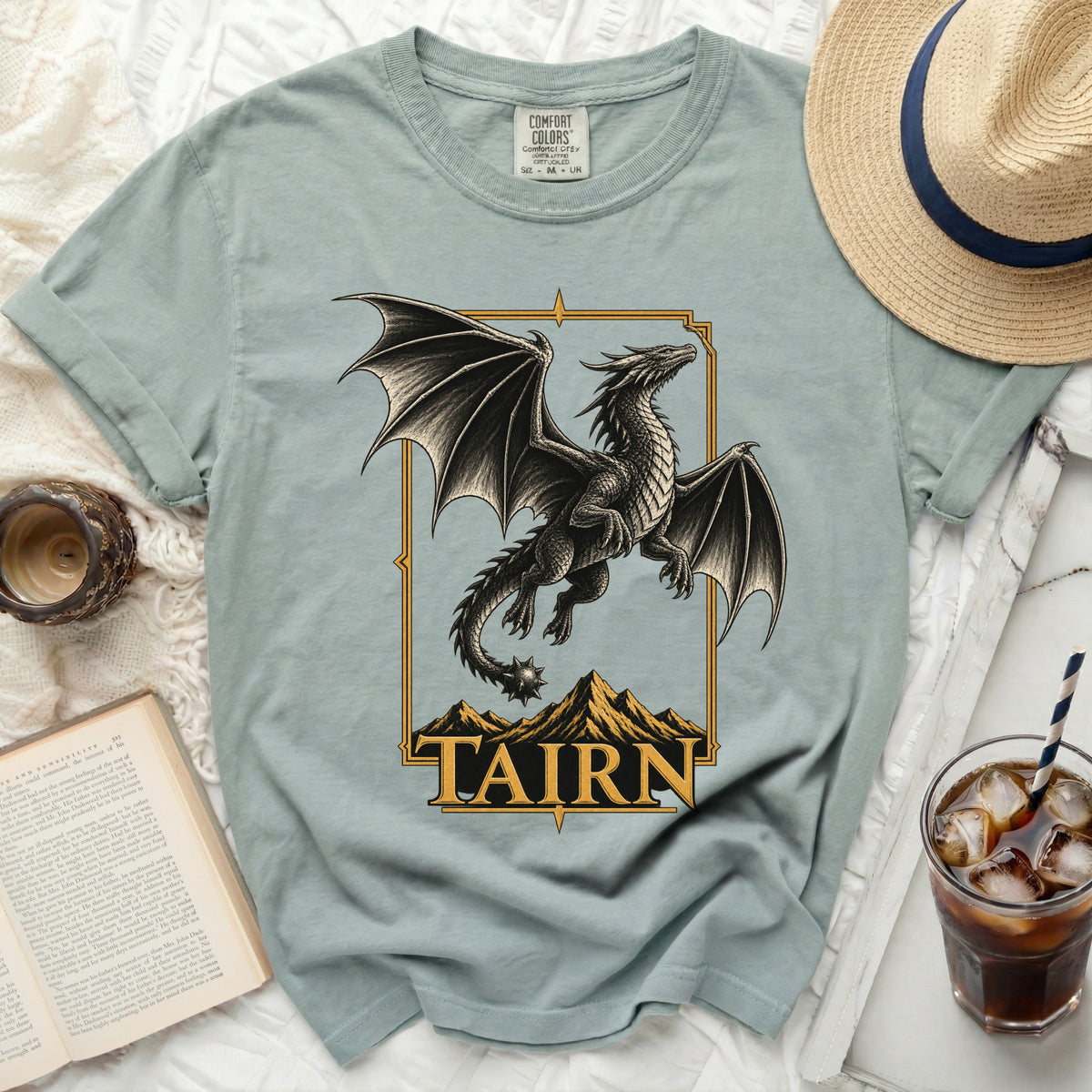 Light blue t-shirt with black dragon graphic and gold border with "TAIRN" text.