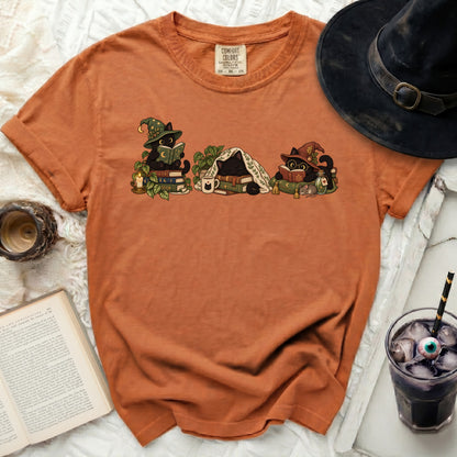 Orange t-shirt with cartoon black cats reading books and wearing witch hats.