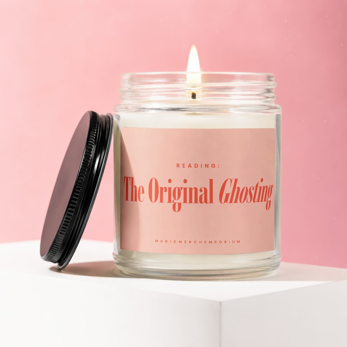 Glass jar candle with lit wick and "The Original Ghosting" text on pink label.