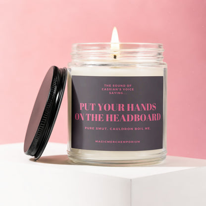 Candle with dark label text "Put Your Hands On The Headboard" on pink background.