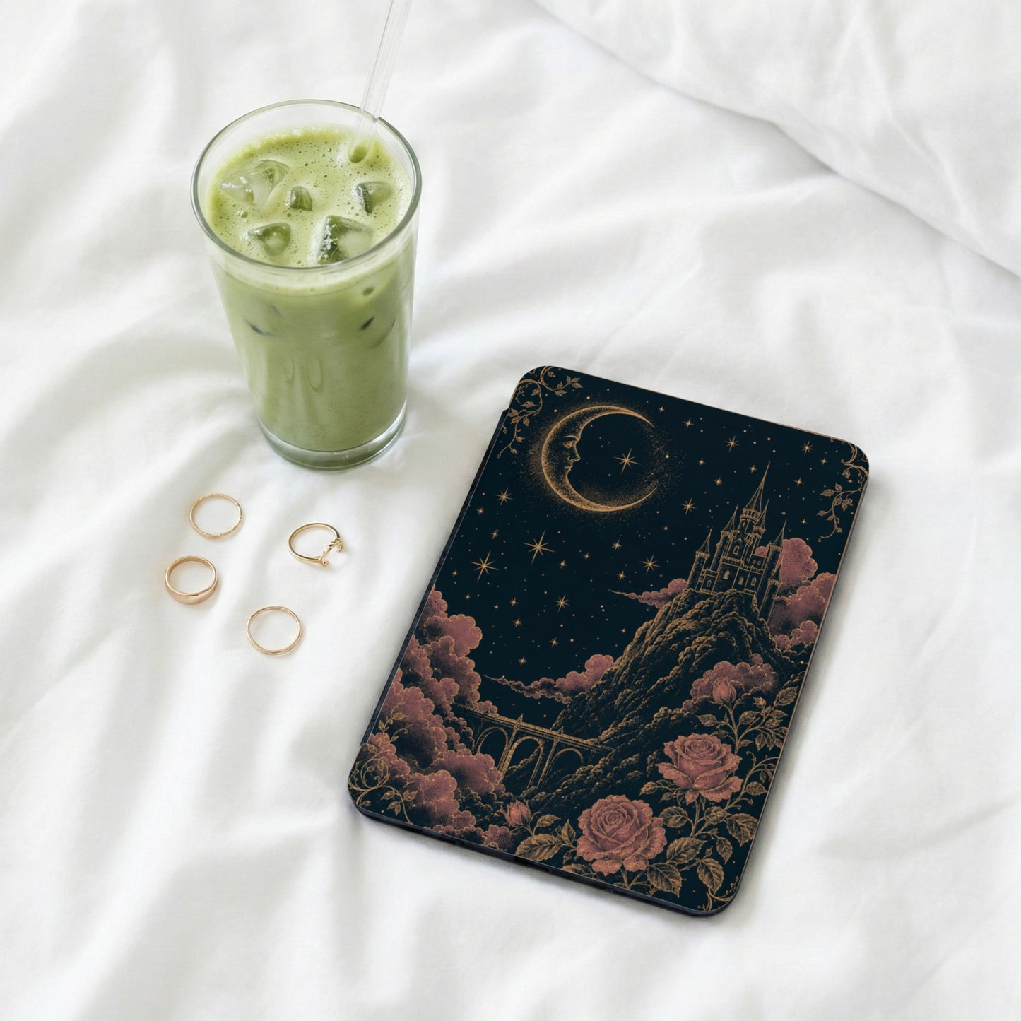 Book with moon and castle, beside a glass of matcha latte and rings.