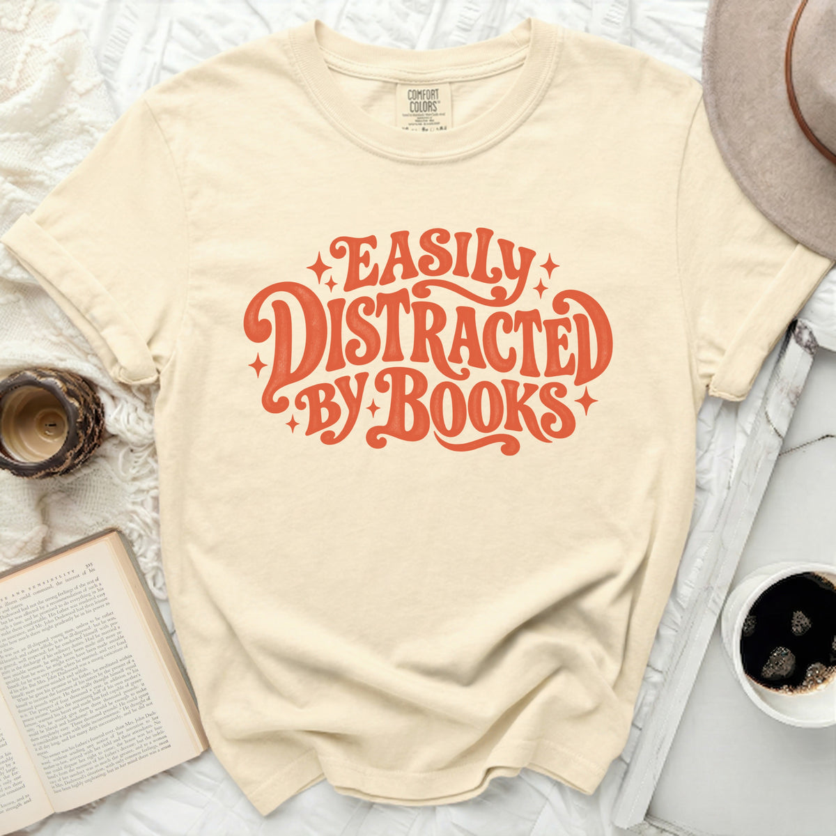 Cream Comfort Colors t-shirt with orange "Easily Distracted By Books" graphic.
