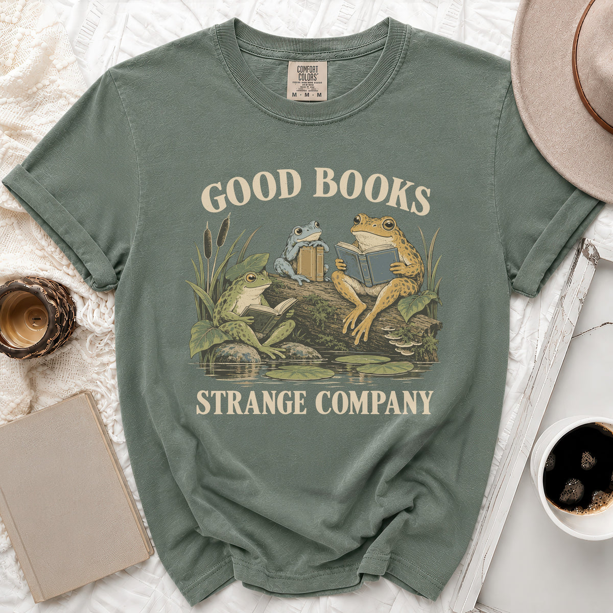 Green t-shirt with "GOOD BOOKS STRANGE COMPANY" text and frogs reading books.