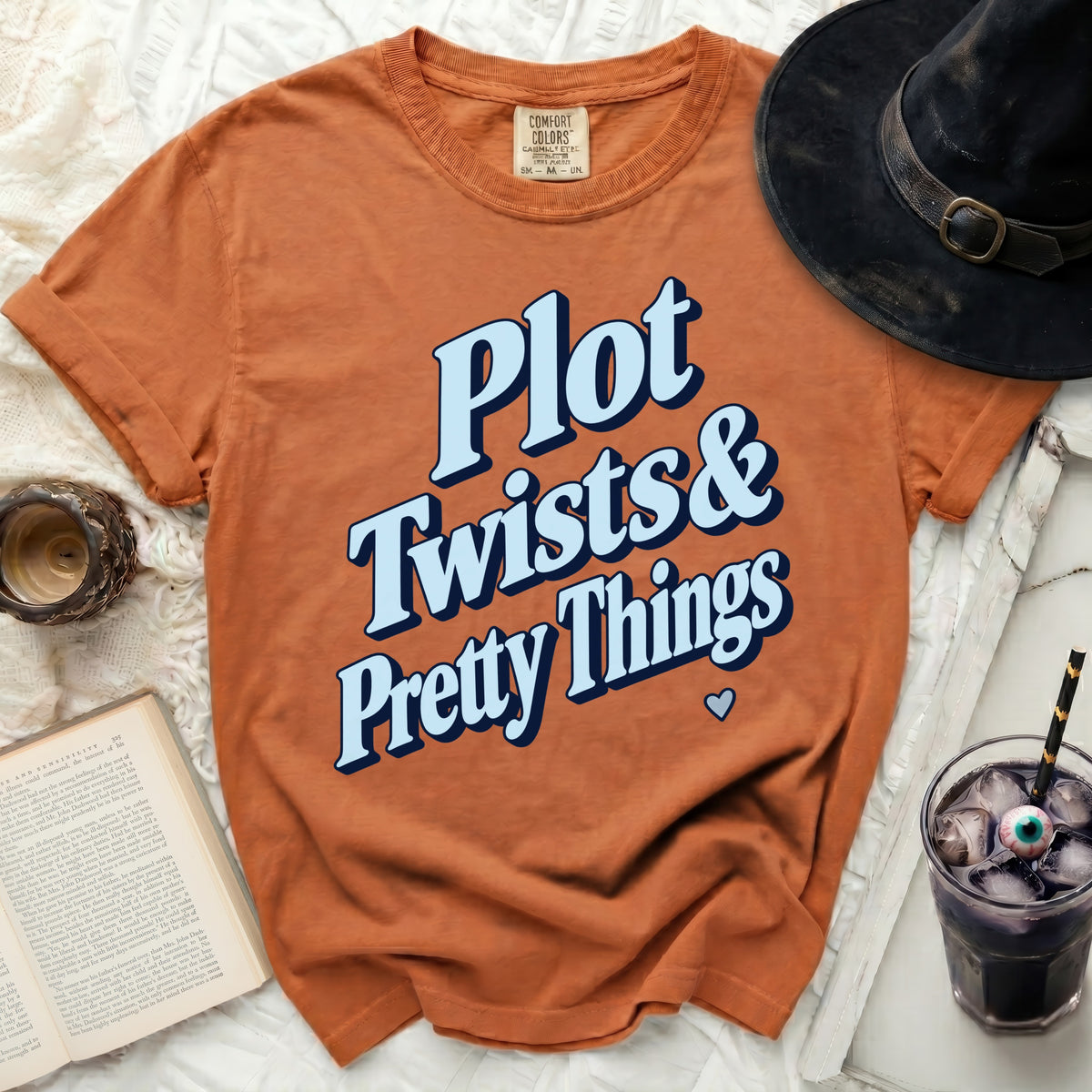 Orange t-shirt with "Plot Twists & Pretty Things" text and Halloween decor.
