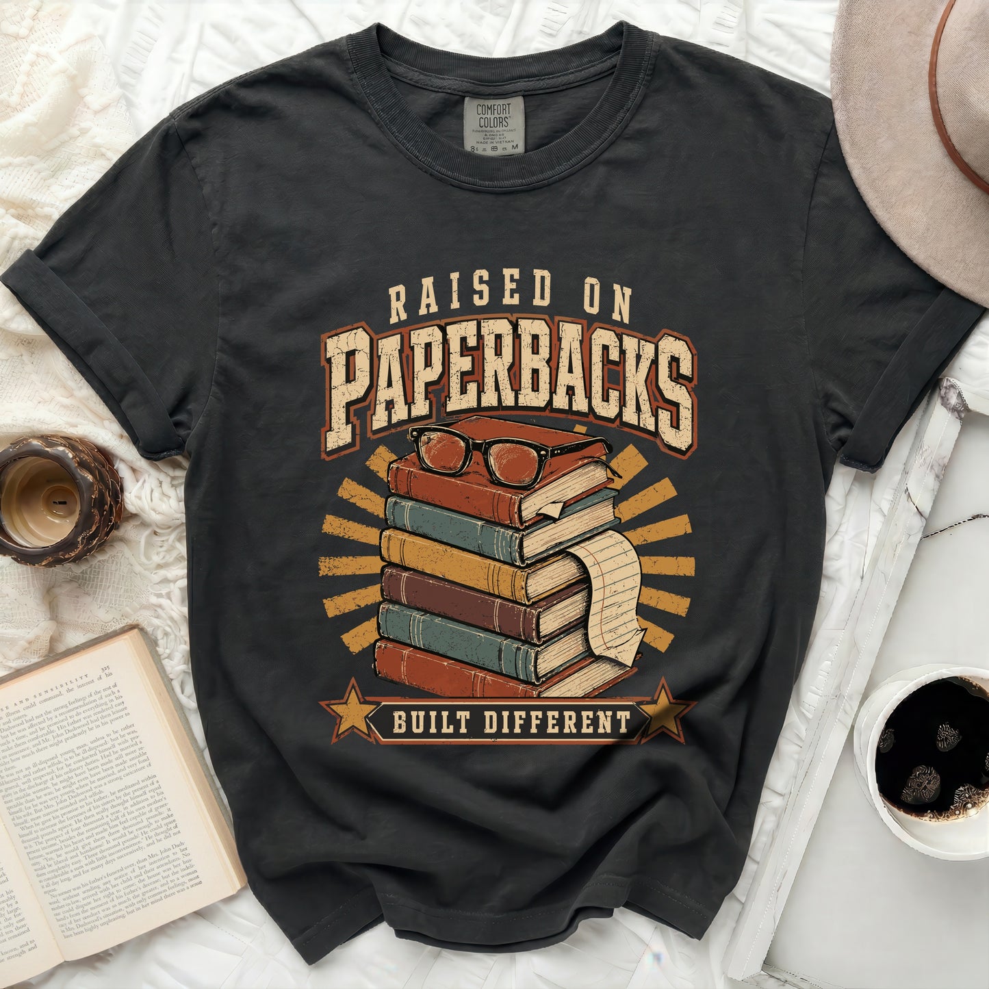 T-shirt with "Raised on Paperbacks Built Different" text and stack of books.