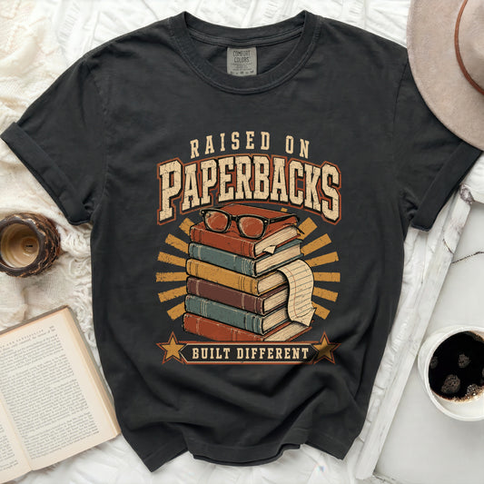 T-shirt with "Raised on Paperbacks Built Different" text and stack of books.