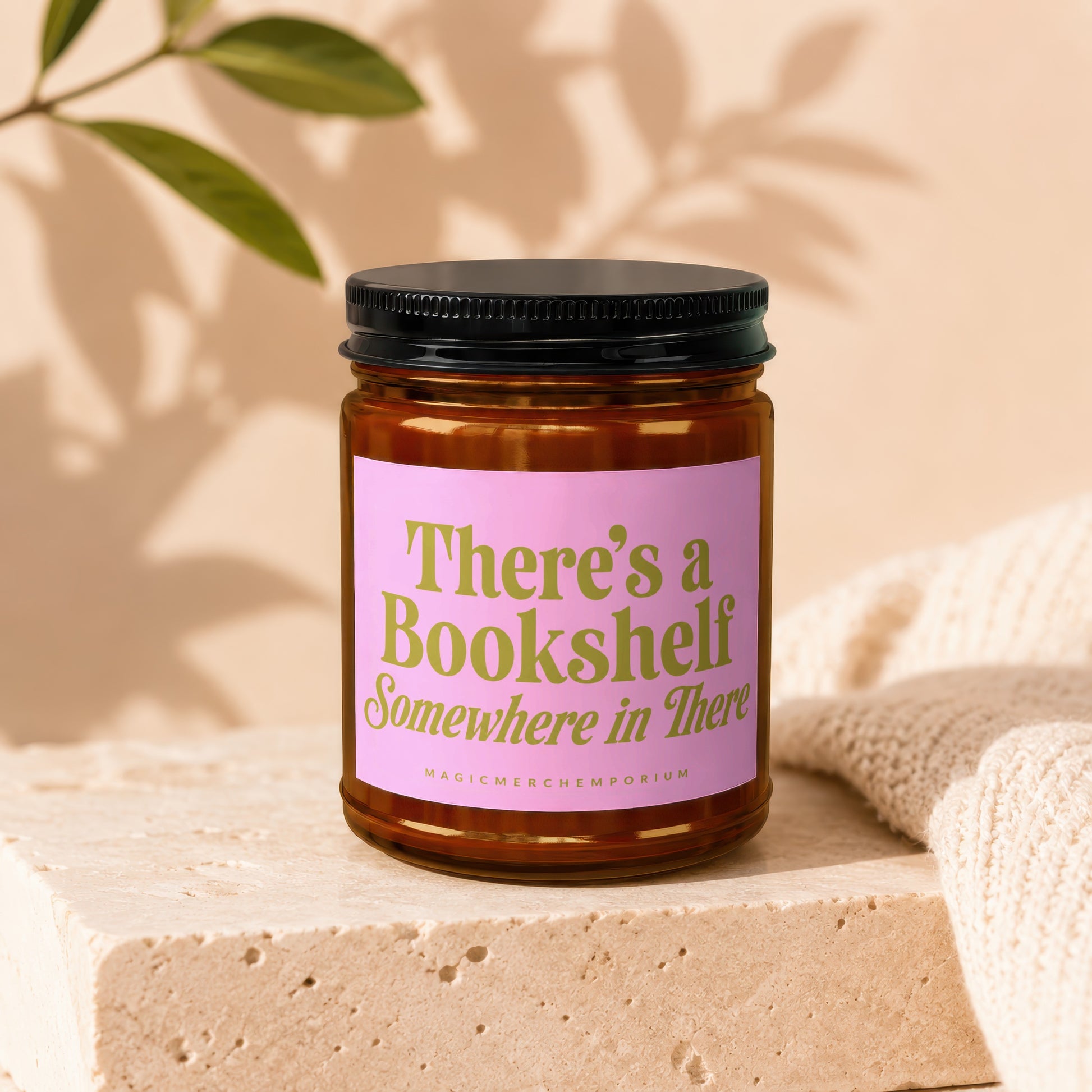Brown glass candle with pink label reading "There's a Bookshelf Somewhere in There".