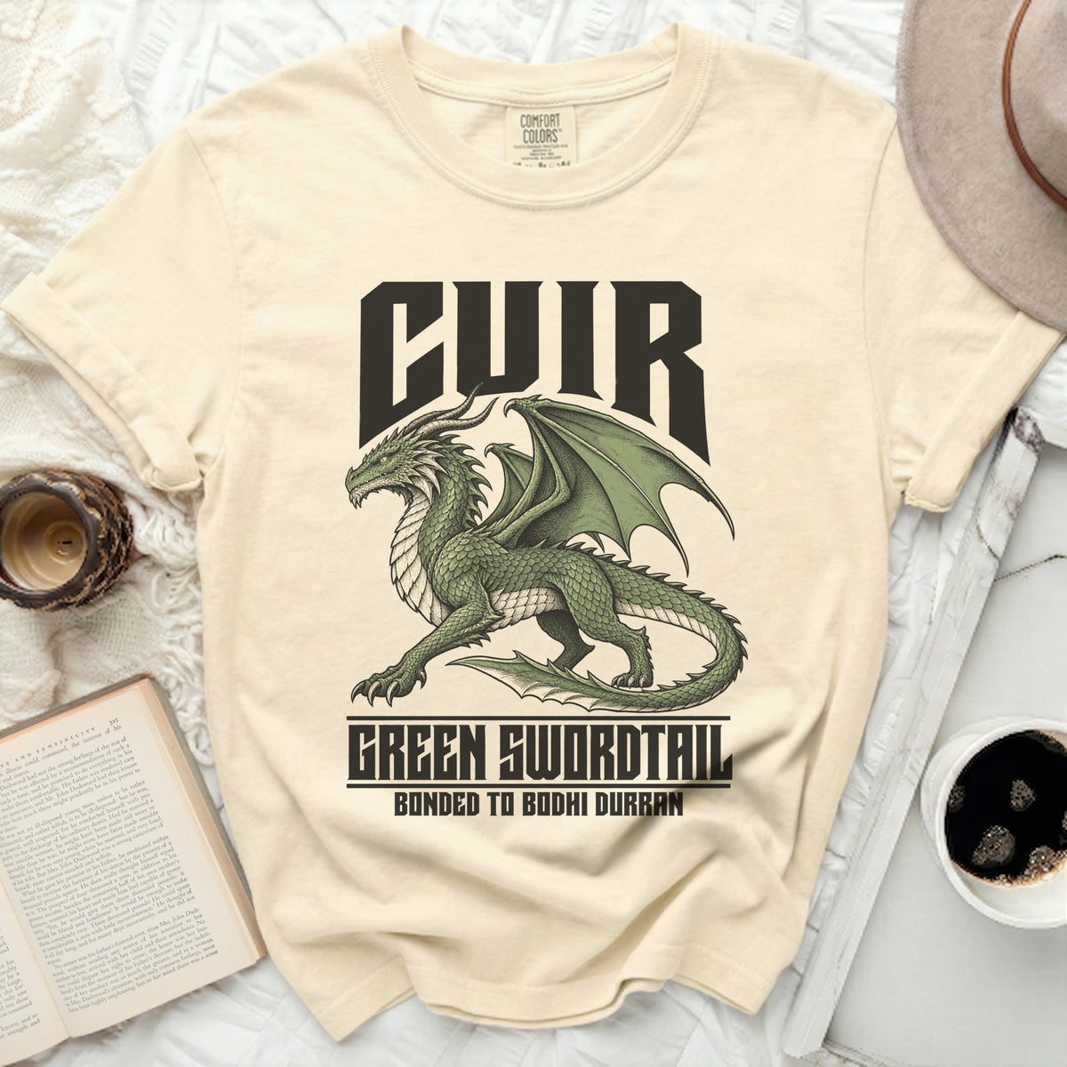 Cream t-shirt with a green dragon graphic and text "CUIR", "GREEN SWORDTAIL", "BONDED TO BODHI DURRAN".