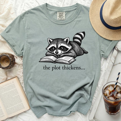 Green t-shirt with raccoon reading a book, "the plot thickens..." text