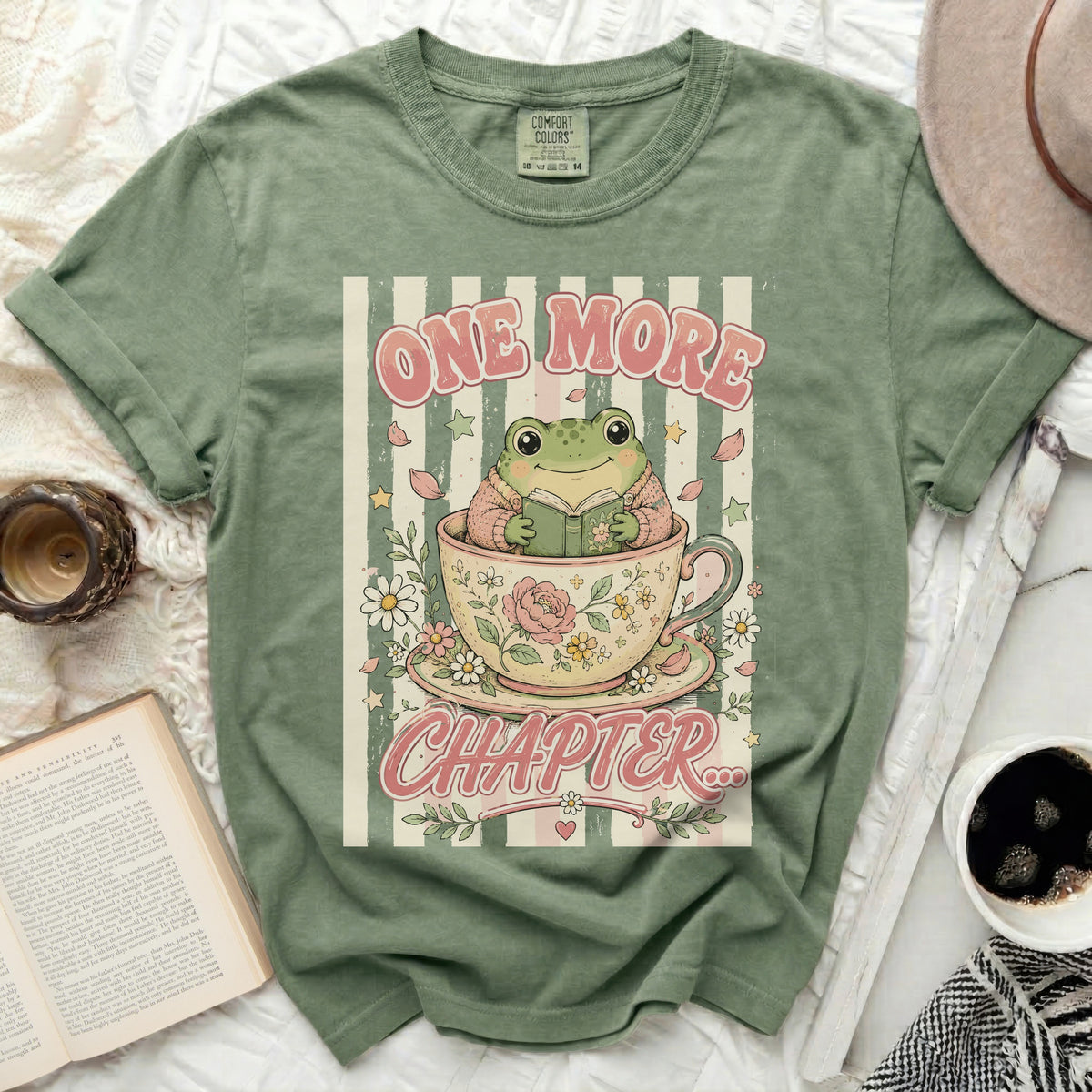 Green t-shirt with a frog reading in a teacup and "ONE MORE CHAPTER" text.