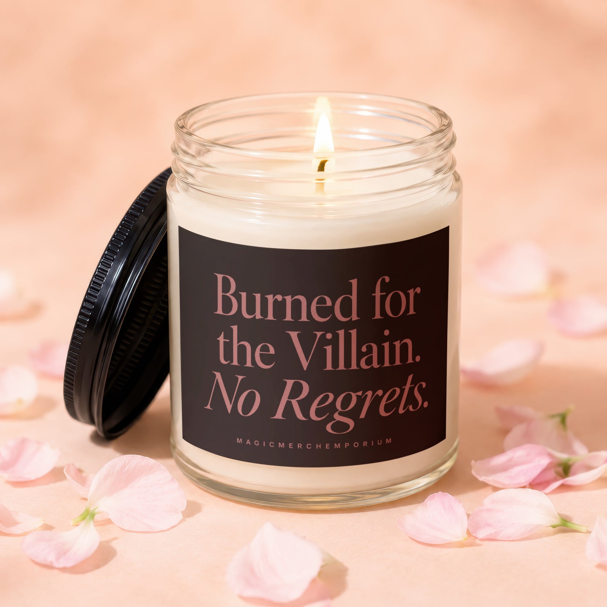 Glass candle labeled "Burned for the Villain. No Regrets." with burning wick.