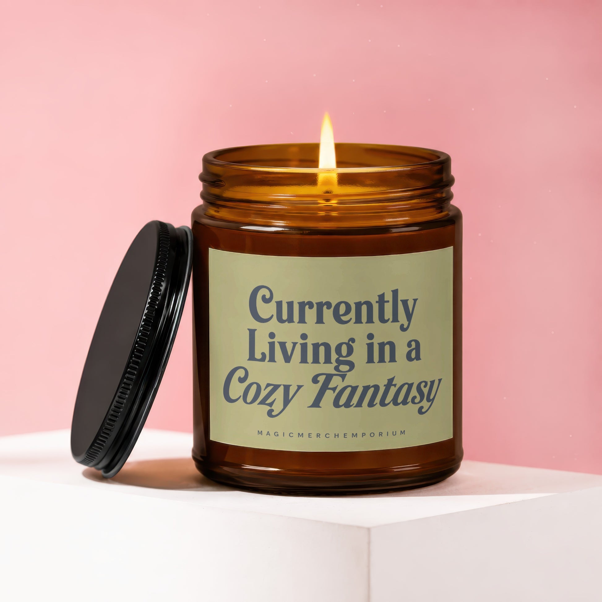 A lit amber candle with the text "Currently Living in a Cozy Fantasy" on the label.