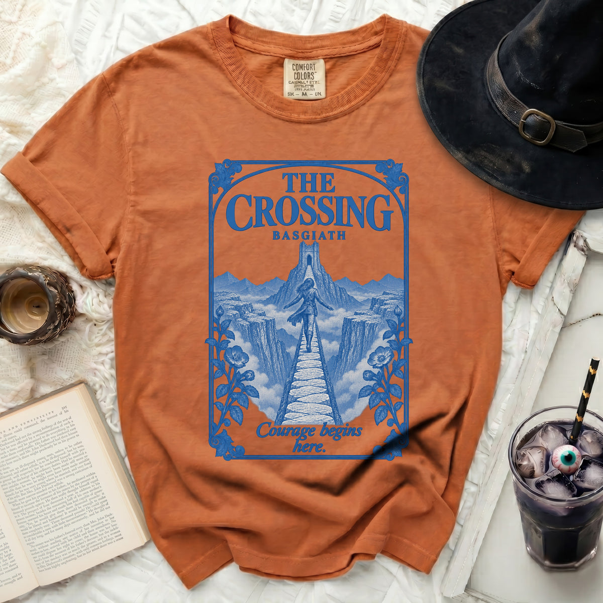 Orange t-shirt with blue graphic design featuring "THE CROSSING BASGIATH" and "Courage begins here."